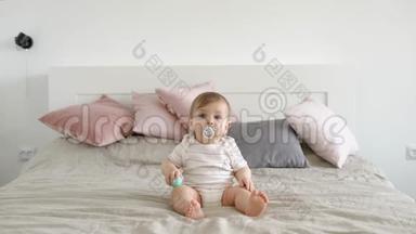 金发碧眼的婴儿坐在一张<strong>大</strong>床上，带着婴儿奶嘴，白天在舒适的家中向前看